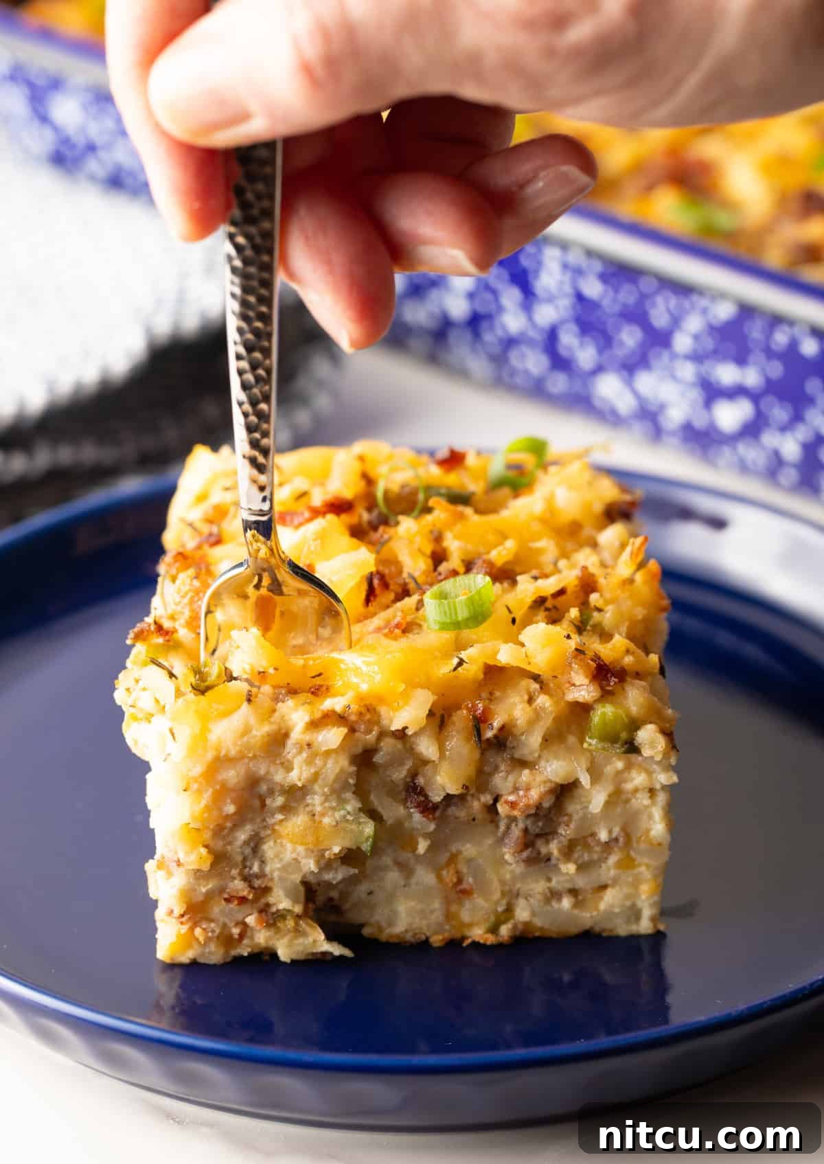 Golden Hash Brown Breakfast Bake 5 A delicious slice of hash brown breakfast casserole on a blue plate, with a fork taking a mouth-watering bite out of it.