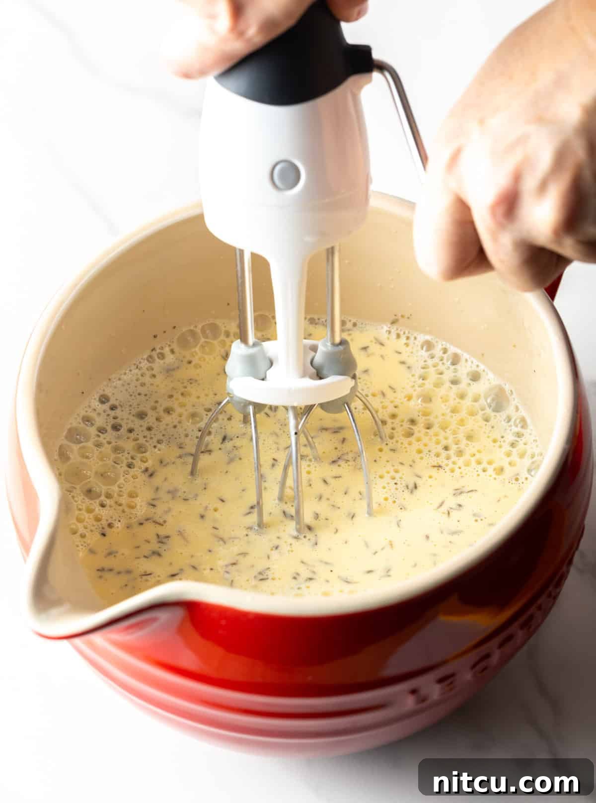 Golden Hash Brown Breakfast Bake 8 A whisk vigorously mixes an egg and cream mixture in a vibrant red bowl, preparing it for the casserole.