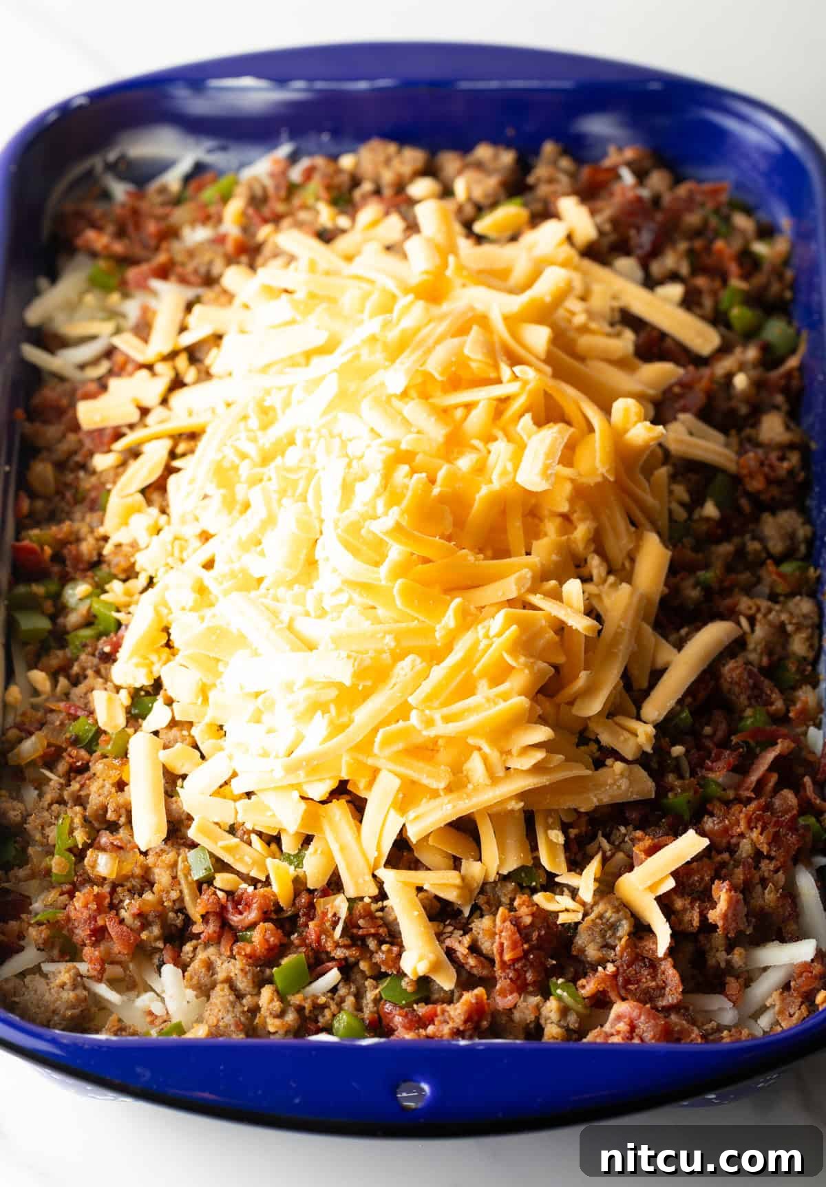 Golden Hash Brown Breakfast Bake 9 Shredded cheddar cheese is being added generously to a casserole dish already filled with layers of hash browns and seasoned sausage.