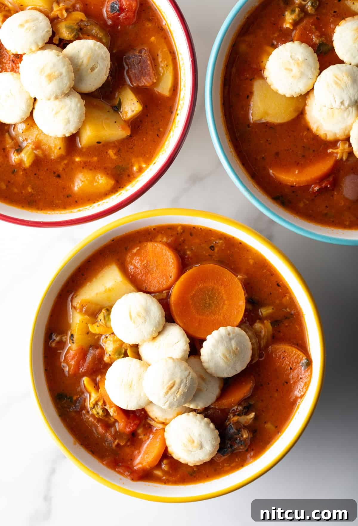 An overhead view of 3 bowls filled with Manhattan-style clam chowder topped with oyster crackers.