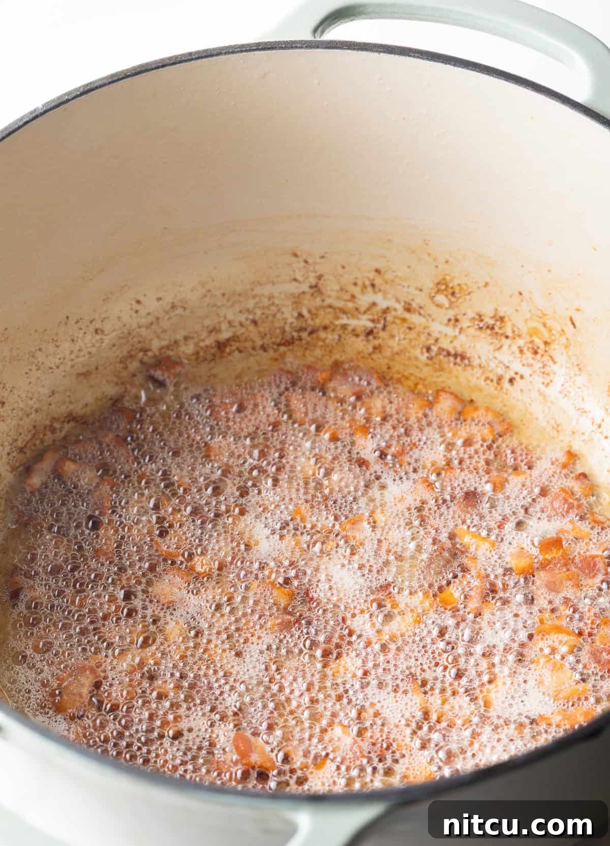 Bacon pieces are being sautéed in a metal pot.
