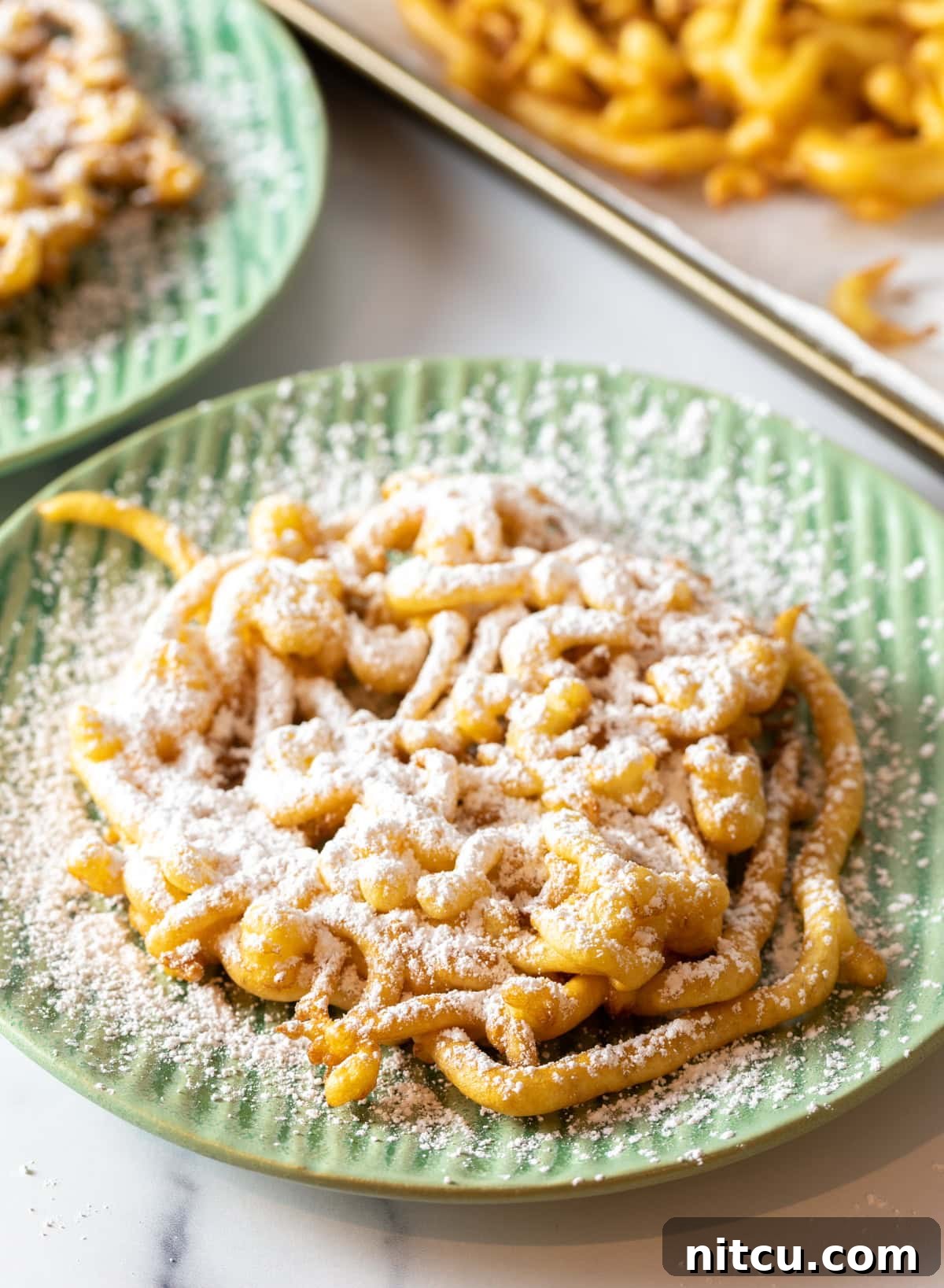 Overhead shot of homemade funnel cake with powdered sugar on a green plate.
