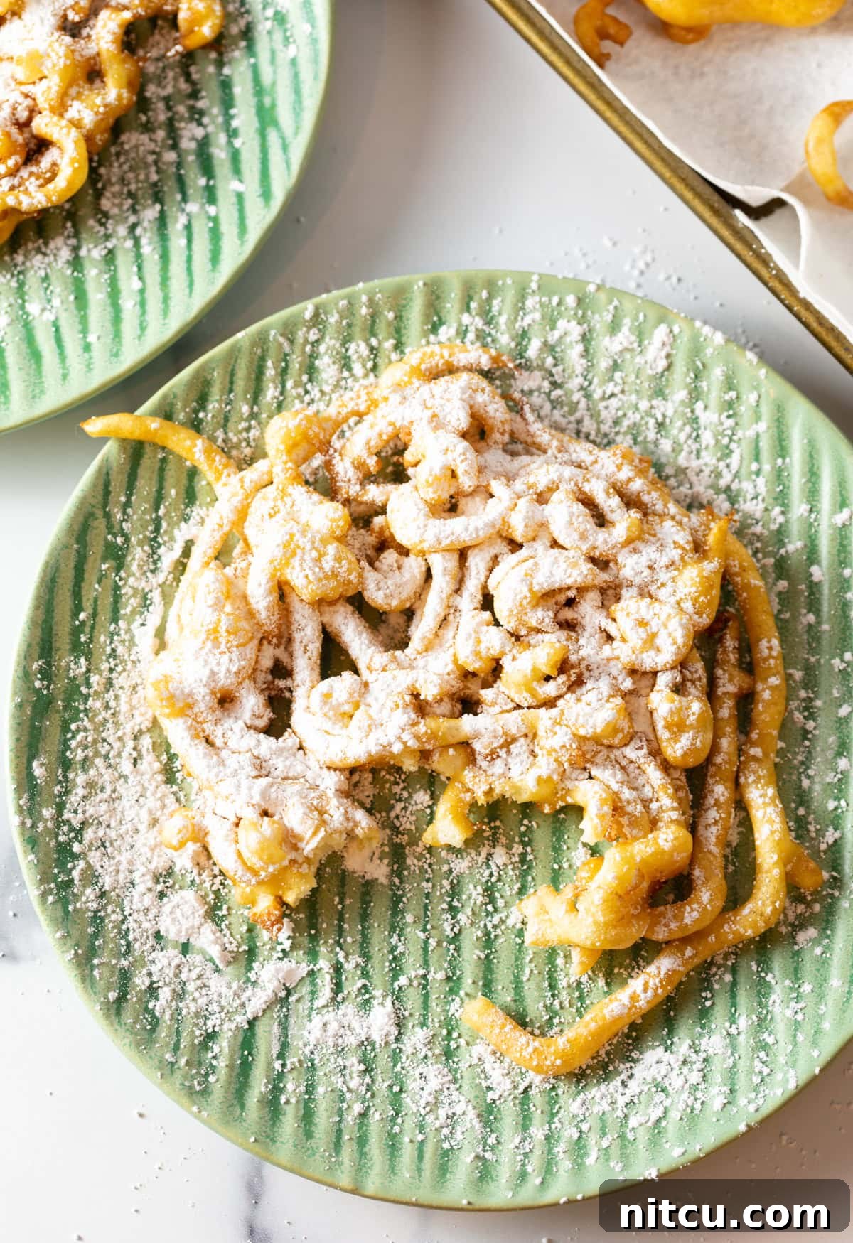 An easy homemade funnel cake recipe topped with powdered sugar, sitting on a green plate with a piece taken out.