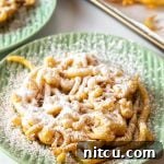 Overhead shot of homemade funnel cake with powdered sugar on a green plate.
