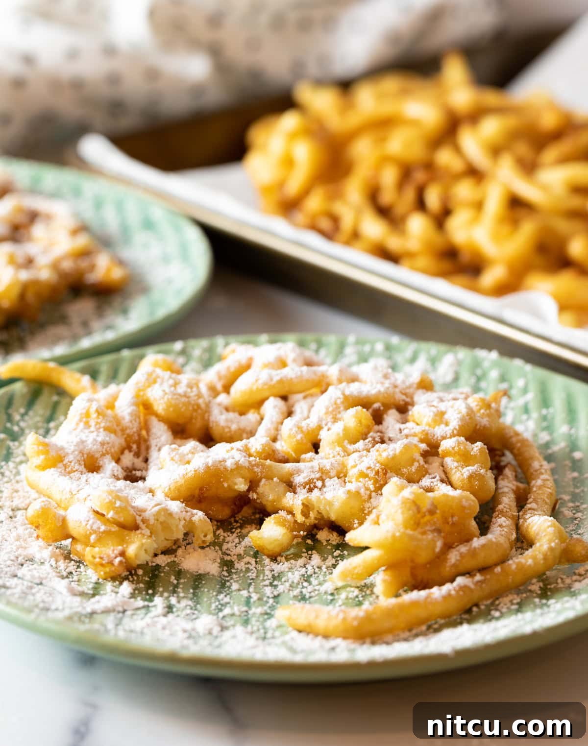Fresh homemade funnel cake topped with powdered sugar, sitting on a green plate with a piece taken out.
