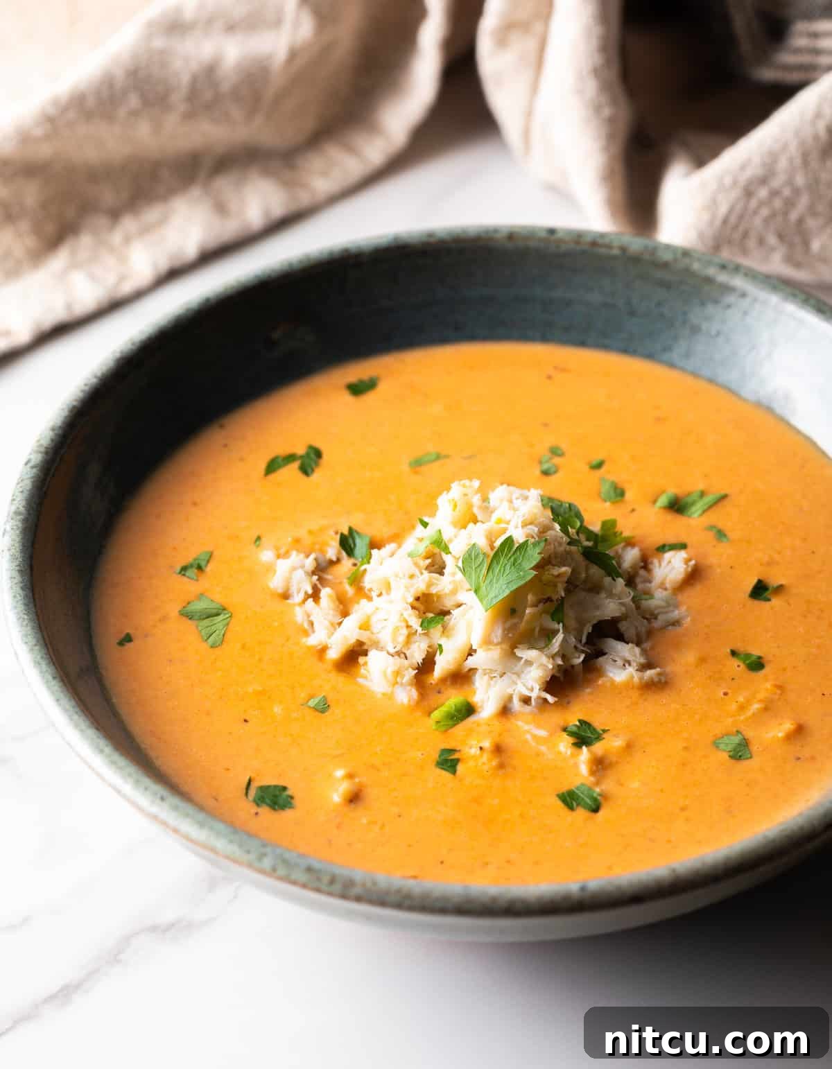 Decadent Crab Bisque 11 A grey bowl filled with a creamy crab bisque soup recipe, with crab meat and parsley on top.