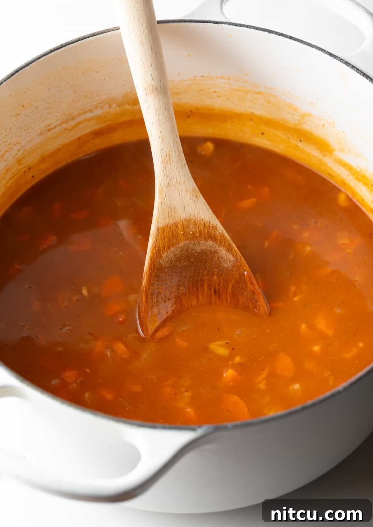 Decadent Crab Bisque 7 A crab bisque soup base is being simmered and stirred in a white pot.
