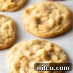 Close up view of three white chocolate macadamia nut cookies on parchment.