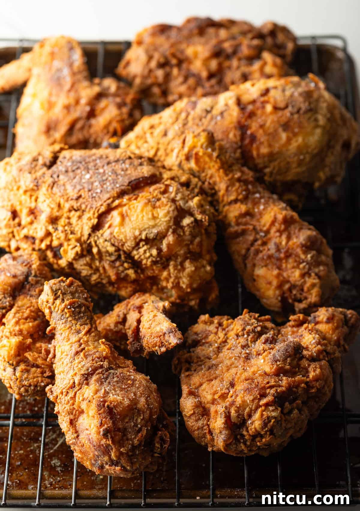 Crispy southern fried chicken cooked in a cast iron skillet draining on a roasting tray.