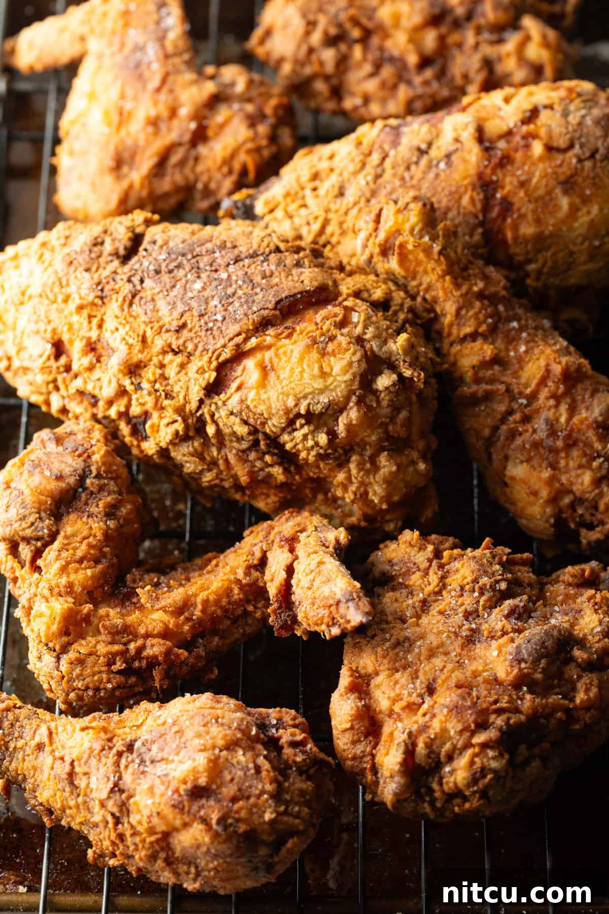 Crispy southern fried chicken cooked in a cast iron skillet draining on a roasting tray.