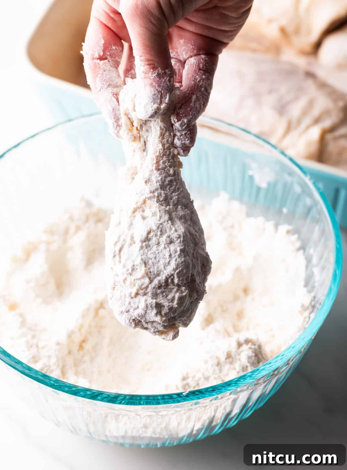 A raw chicken wing is being dredged in a flour mixture for Southern fried chicken.