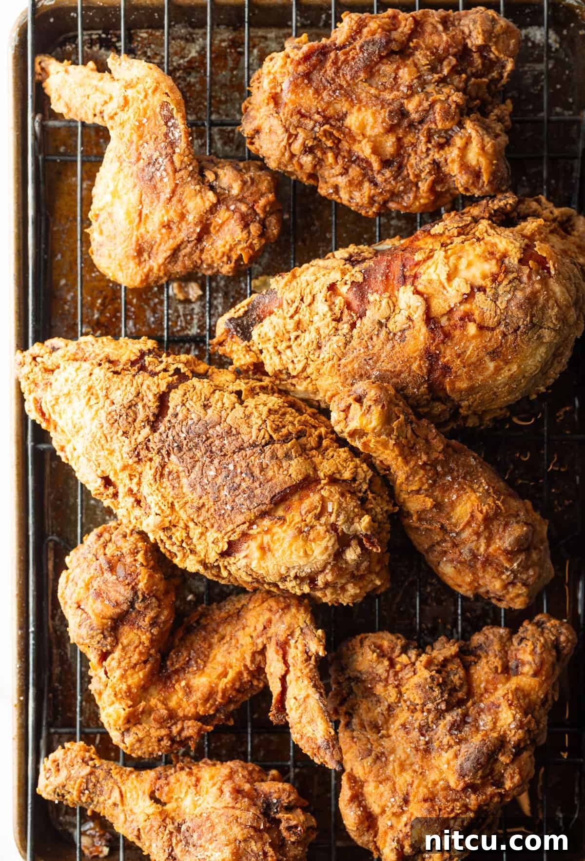 Crispy southern fried chicken cooked in a cast iron skillet, draining on a drying rack.