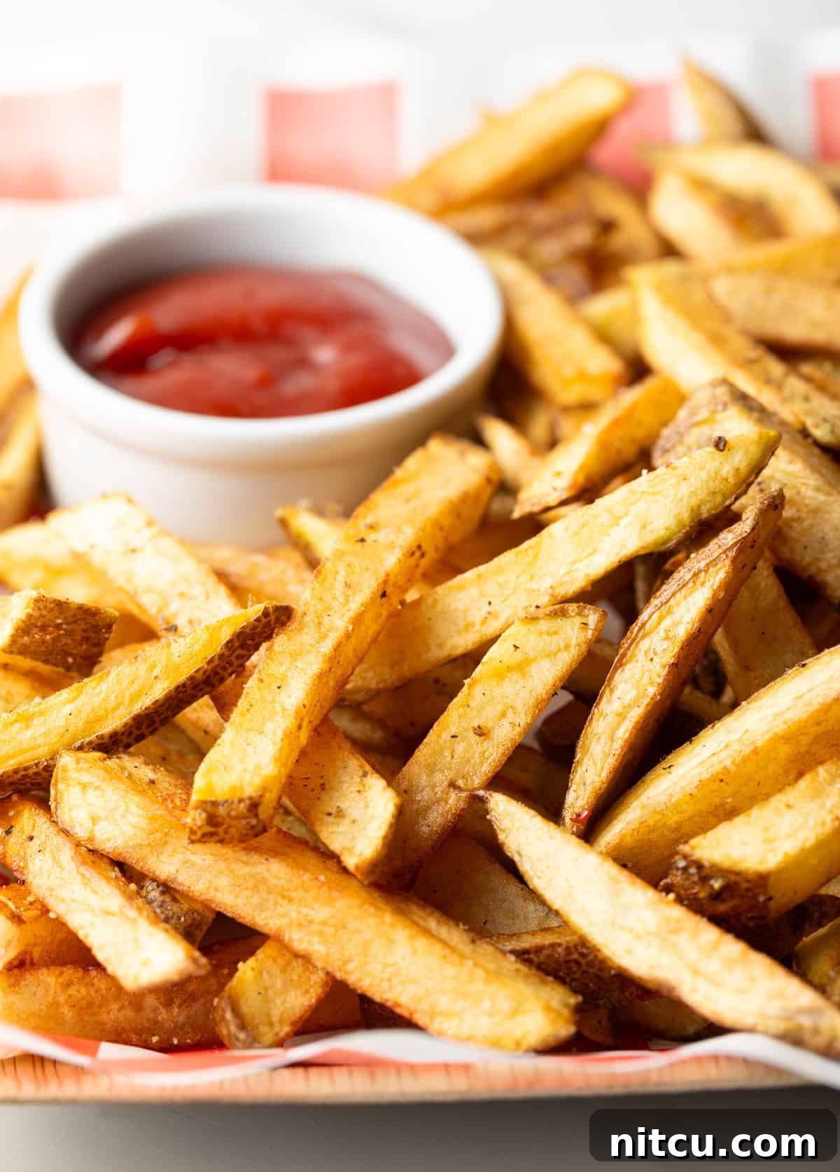 Red and white checkered basket loaded with homemade french fries and ramekin of ketchup.