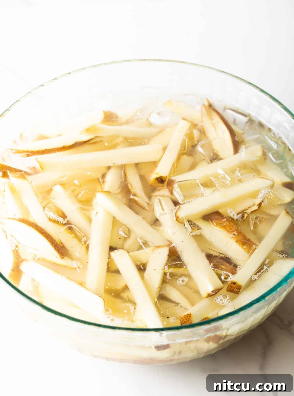 Slices of raw potato in a large glass bowl of water.