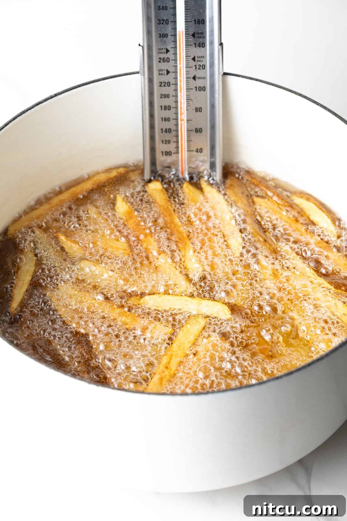 Boiling thick slices of potatoes in a white pot of oil, with a thermometer clipped on the side.