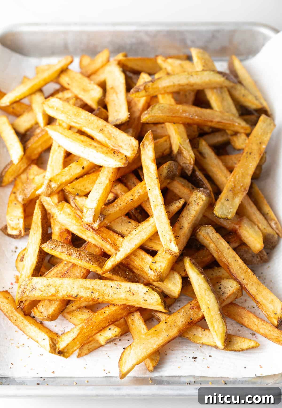 Top down view freshly fried potatoes in a pile on a baking sheet.