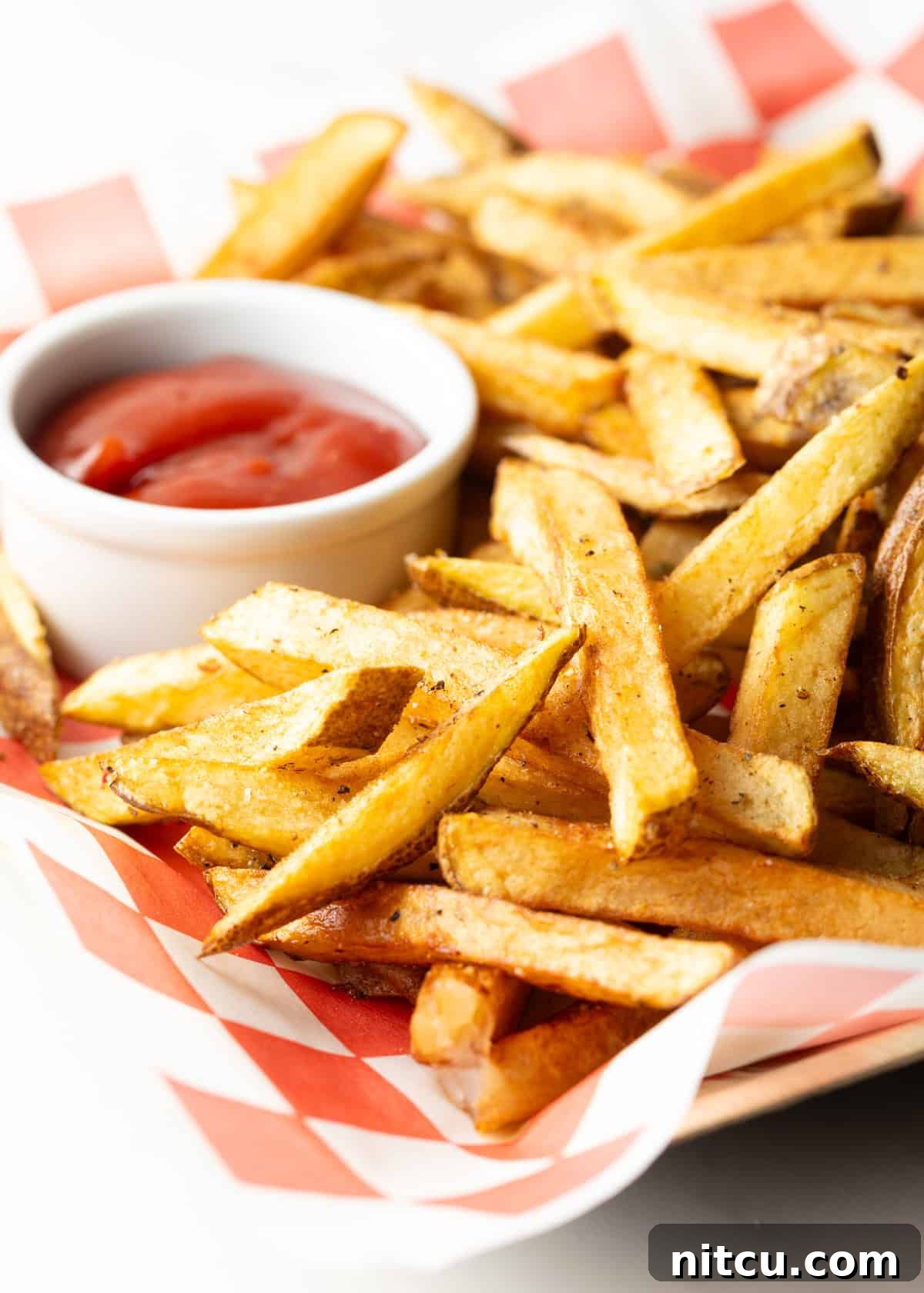 Red and white checkered basket loaded with homemade french fries and ramekin of ketchup.