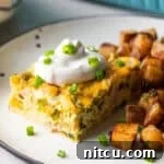 A slice of baked Denver omelet casserole topped with sour cream, next to a serving of home fries on a white plate.