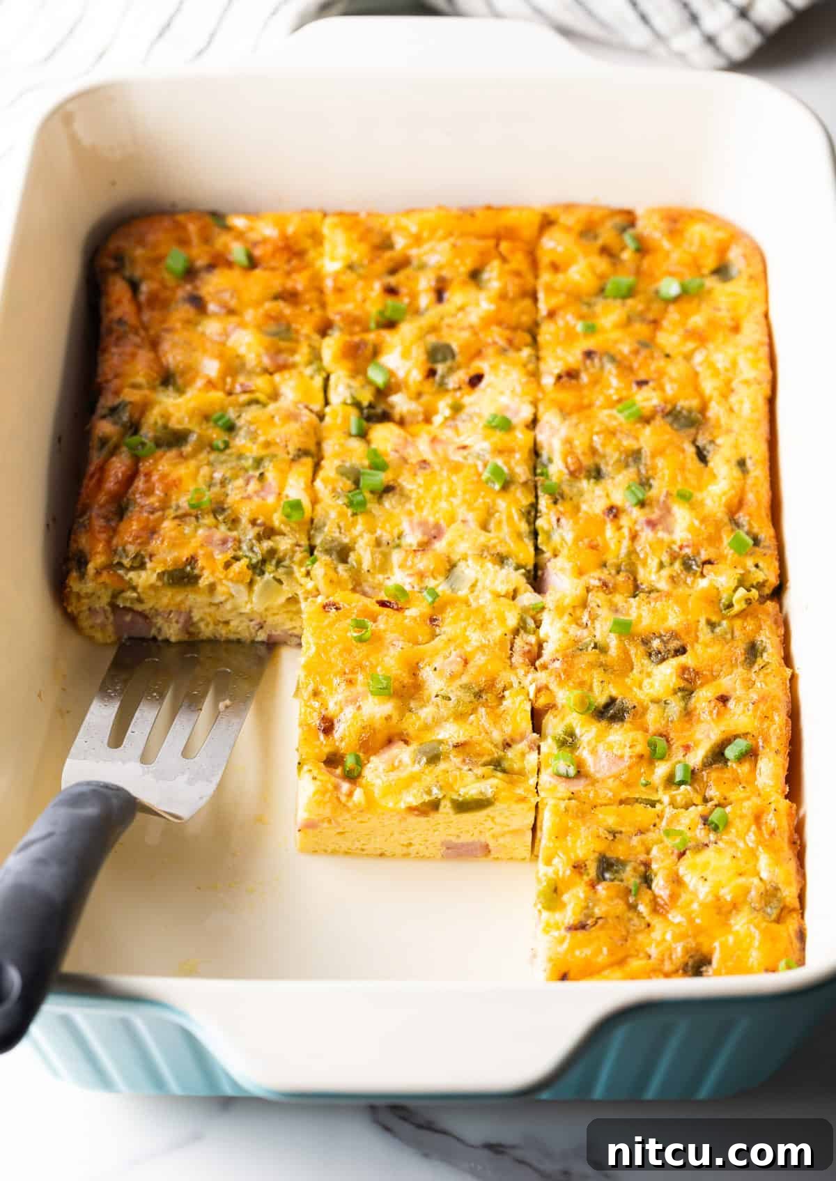 Mile-High Breakfast Casserole 3 Pre-sliced western omelette casserole in a white baking dish, with a metal spatula ready for serving.