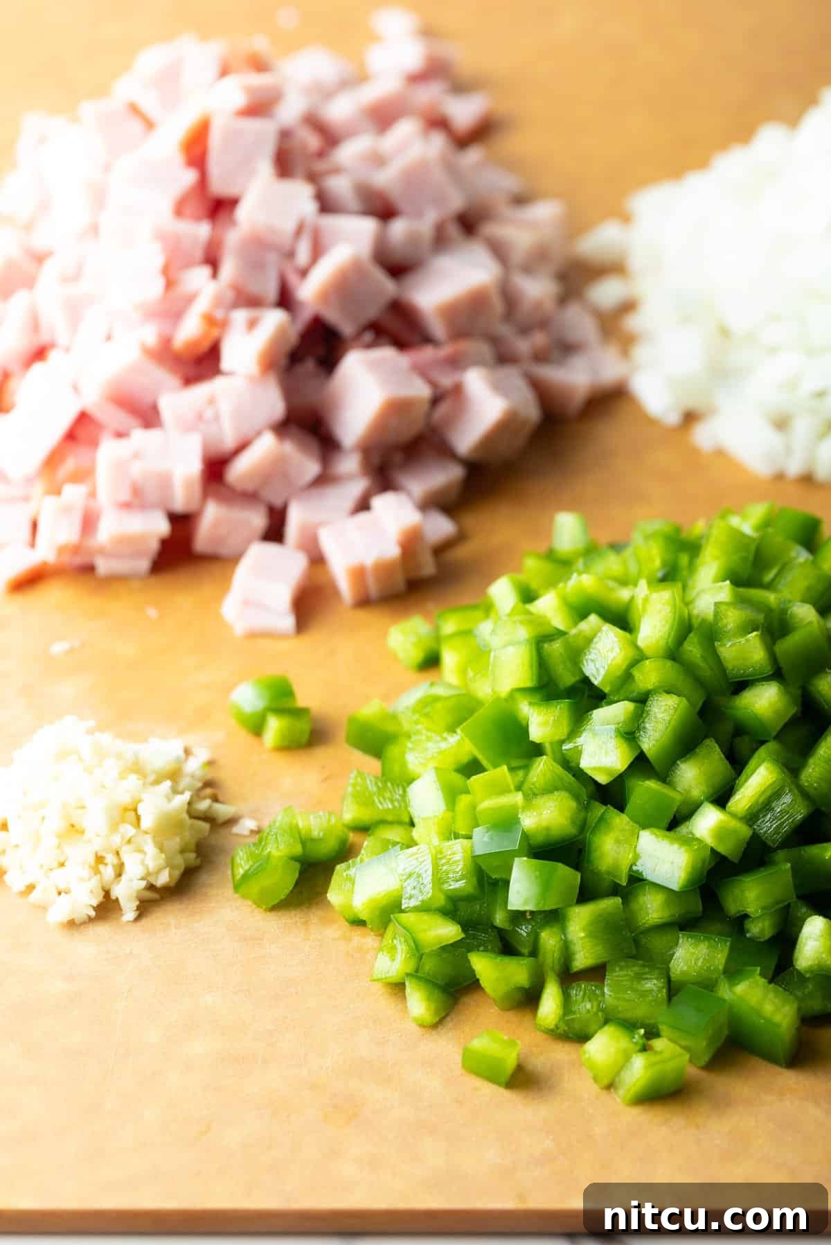 Mile-High Breakfast Casserole 6 Dice ham, green bell peppers, and garlic sitting in piles on a wooden cutting board.