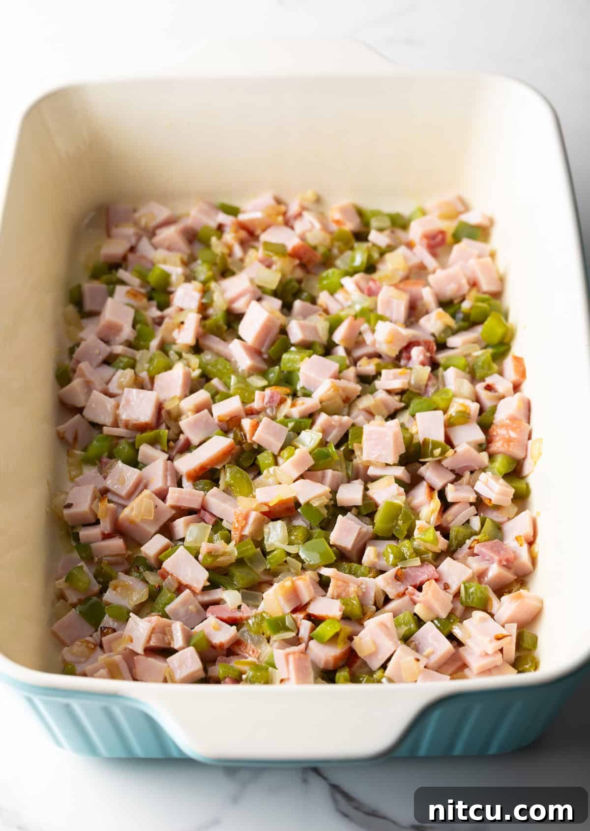 Mile-High Breakfast Casserole 8 Cubed ham and diced veggies layered at the bottom of a white baking dish.