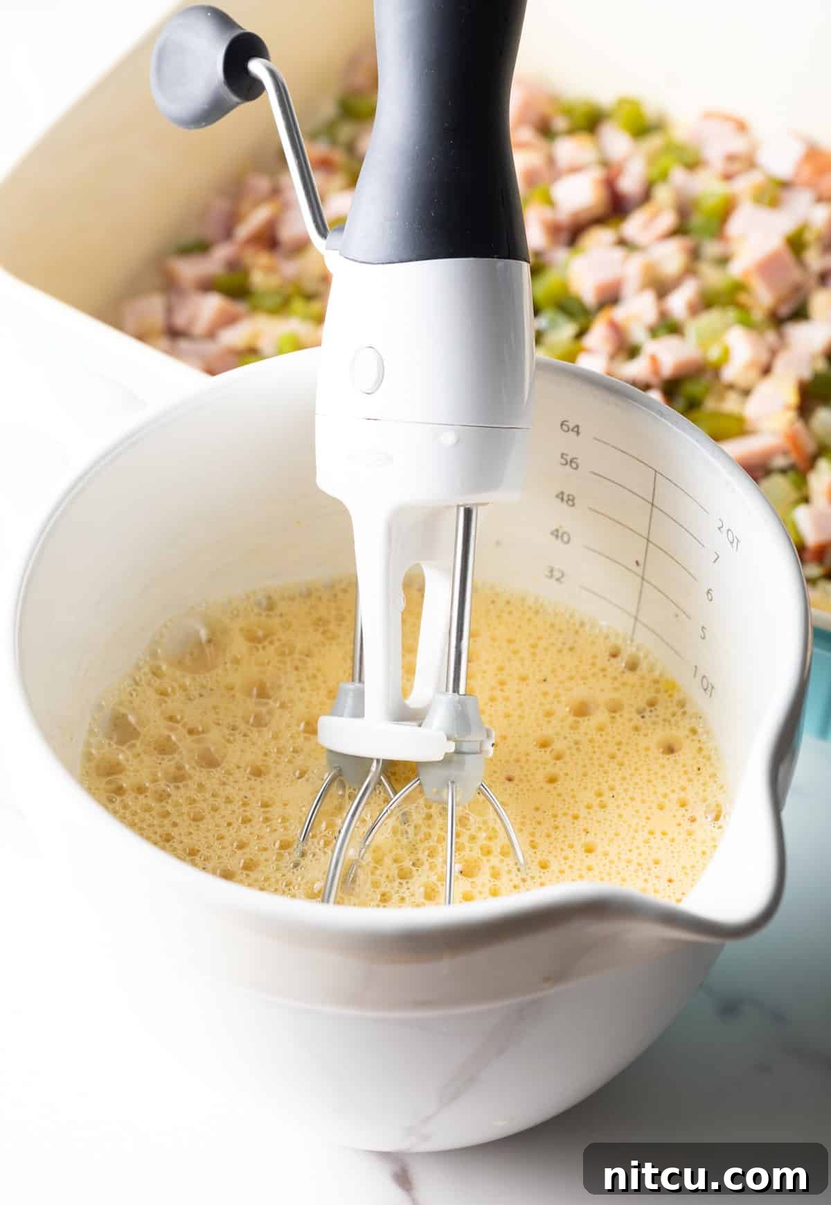 Mile-High Breakfast Casserole 9 An egg and cream mixture is being whisked together in a white measuring bowl.